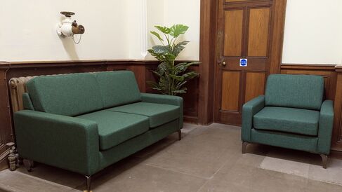 A large green sofa and a smaller green armchair on a stone floored landing
